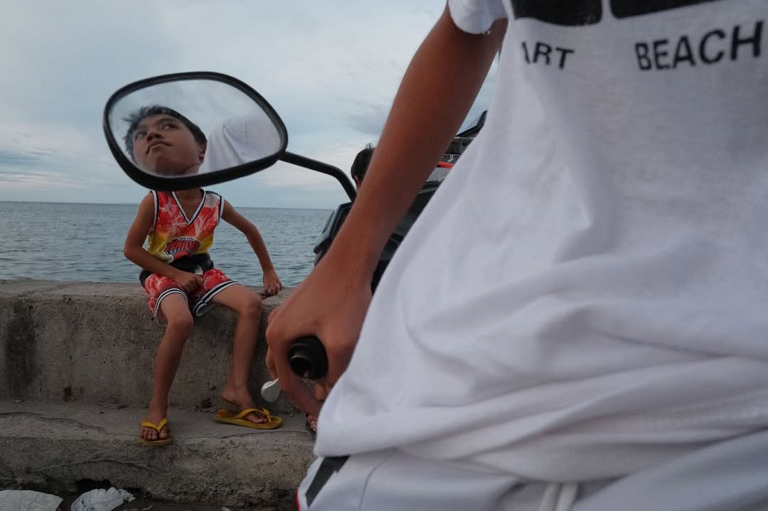 Artist Spotlight: “Catch A Moment” by @hersleyvencasero

This weeks Artist Spotlight features Hersley-Ven Casero, multidisciplinary visual artist and photographer based in Dumaguete City, Philippines. His long-term series, “Catch A Moment” moves through everyday streets and fleeting glances, finding honesty in the uncanny moments that make us deeply human.

“These photographs are not about perfection. They are about presence. I’m chasing a feeling: the rush of kids mid-air above the sea, the hush of light falling through a window, a dog silhouetted against a golden sky, kids playing atop sacks of crimson onions, glowing like jewels, a woman’s face caught twice in one moment, real and reflected. Every frame is a quiet witnessing, a heartbeat stilled in time.

Drawn to the poetry of the everyday, I look for the magic in the mundane: in the warmth of sunlit walls, in shadows cast by strangers, in the choreography of street life unfolding without warning. This is where stories live, where life pulses loudest in its smallest, most honest gestures.

Catch A Moment is my way of honoring what most might walk past. It is not about capturing the perfect shot. It is about capturing the true one, the kind that stirs something in you, the kind you feel before you fully see.”